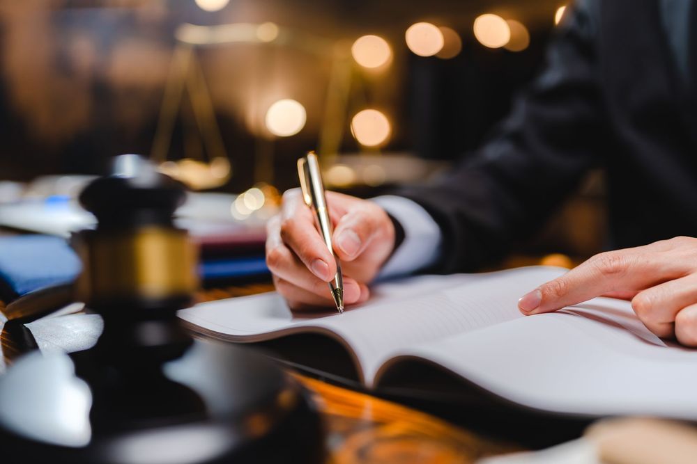 A person is sitting at a table writing in a notebook with a pen.
