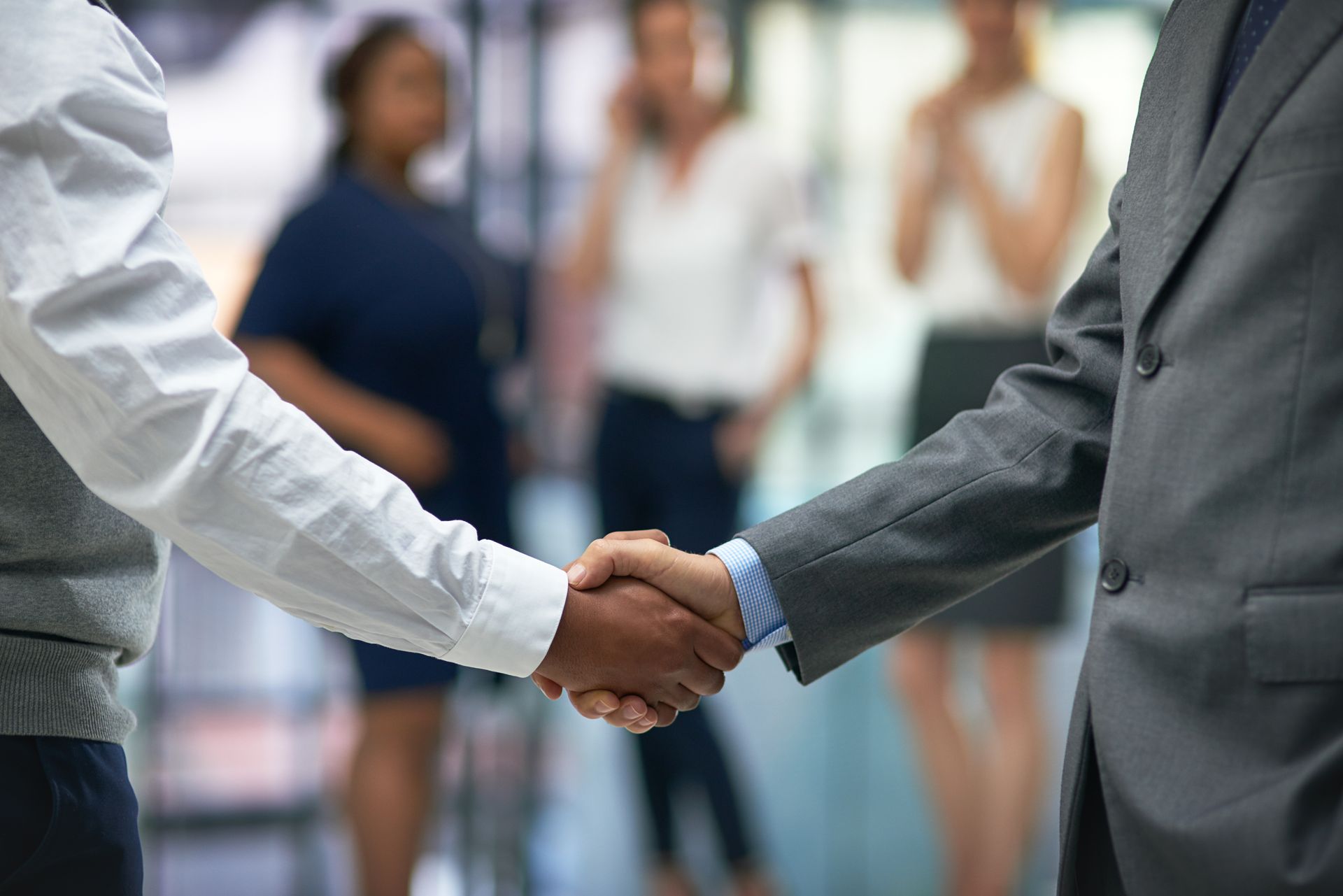 Two men are shaking hands in front of a group of people.