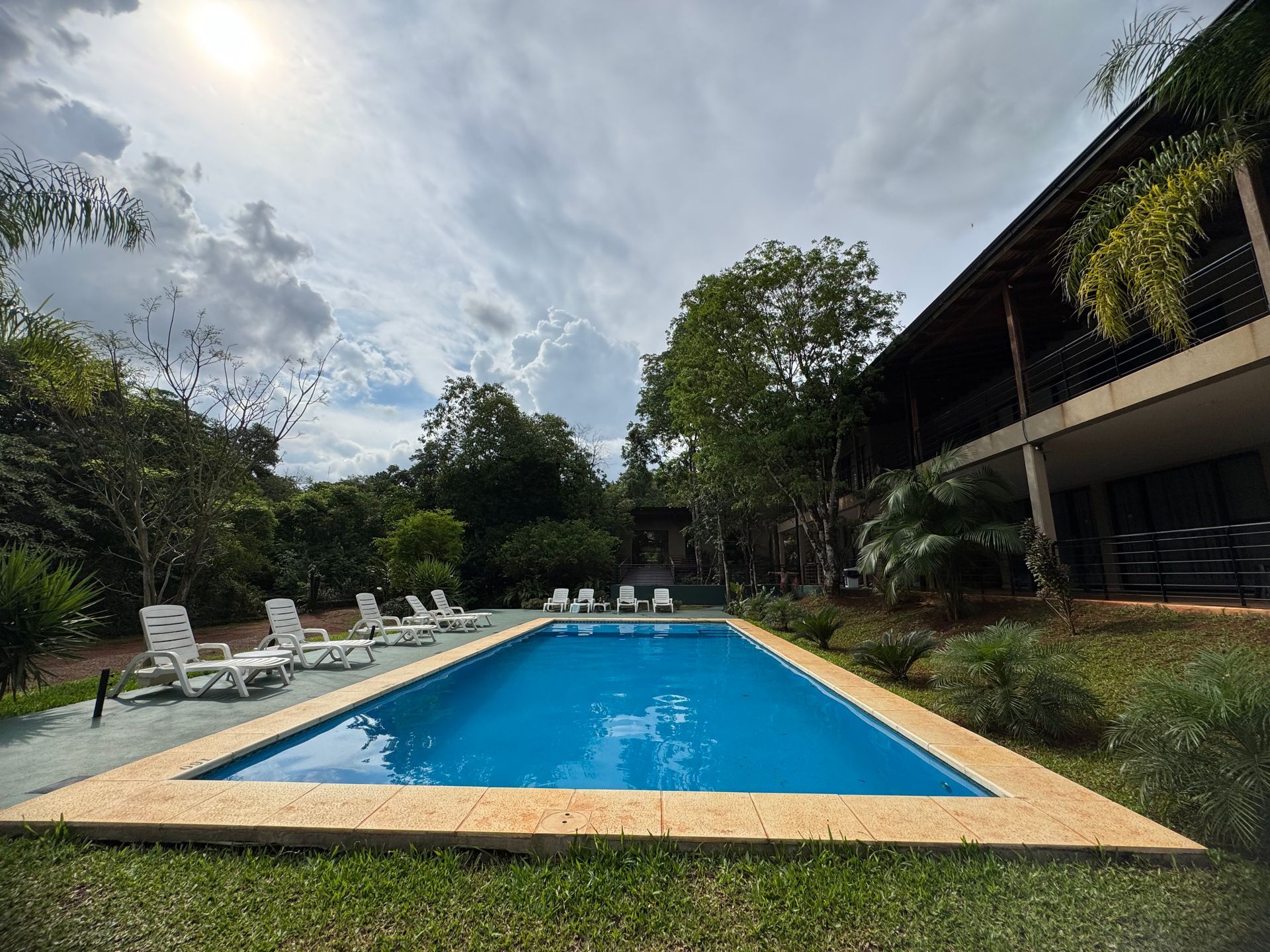 A large swimming pool surrounded by chairs and trees in front of a building.