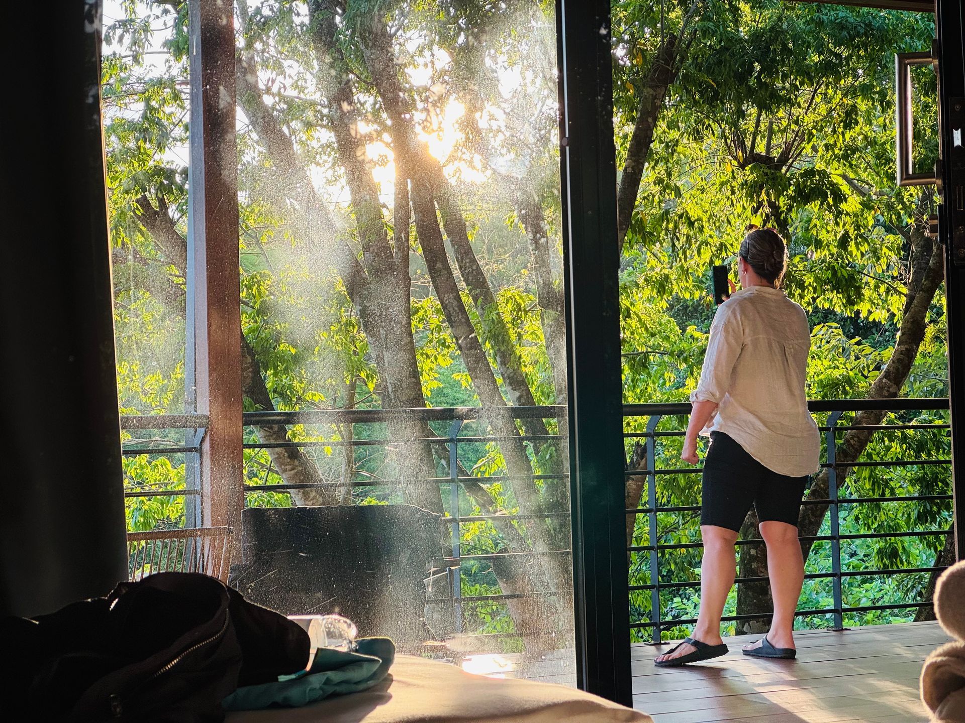 A woman is standing on a balcony looking out at the trees.