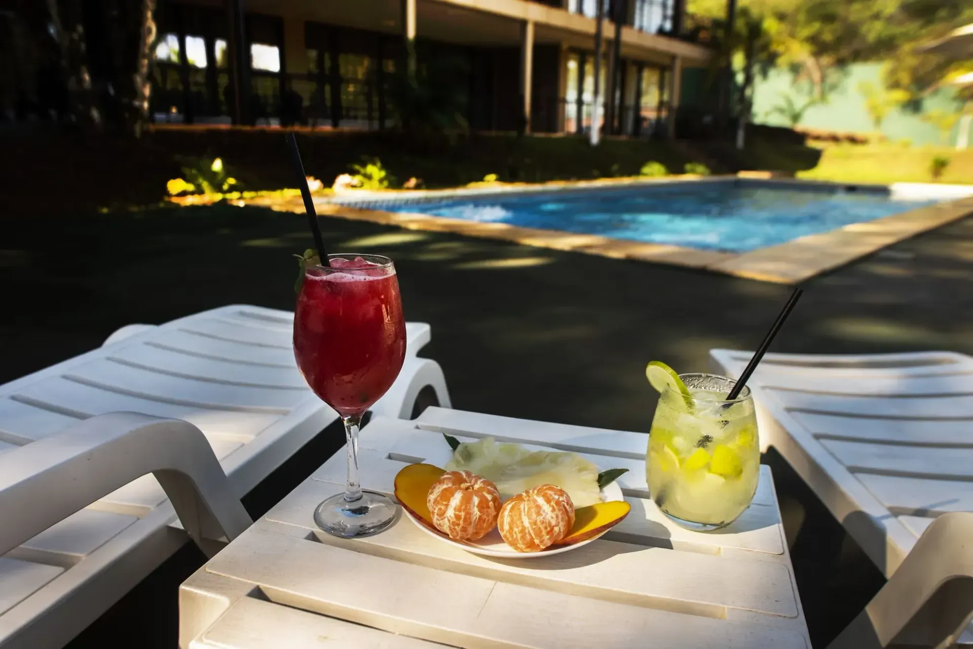 Two drinks are on a table in front of a swimming pool