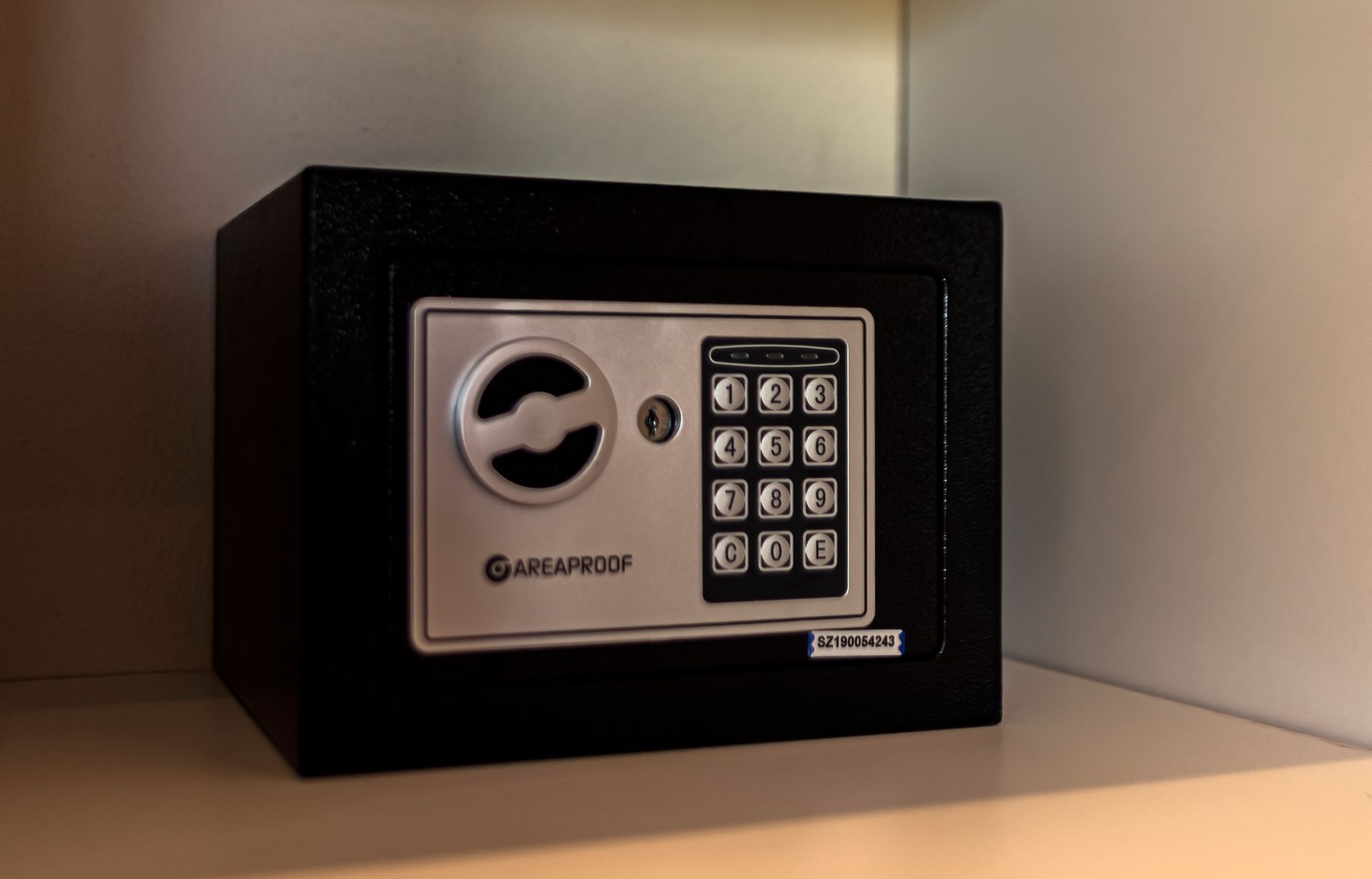 A black electronic safe is sitting on a white shelf.