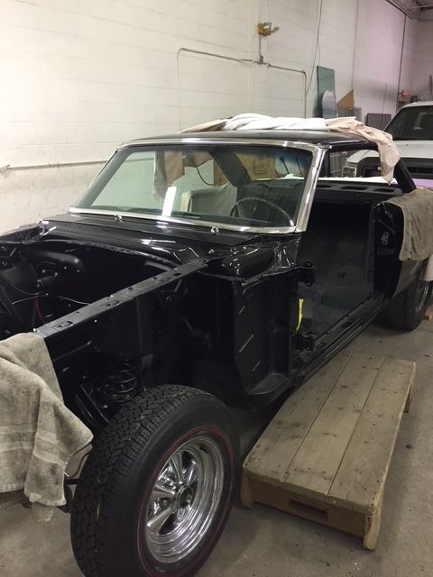 Black classic car in a shop, partially restored, with red-line tires.