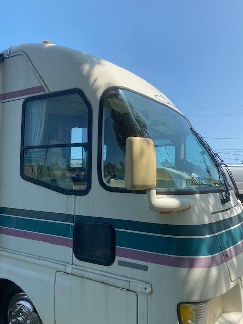 Tan RV with teal and purple stripes, parked on a sunny day.