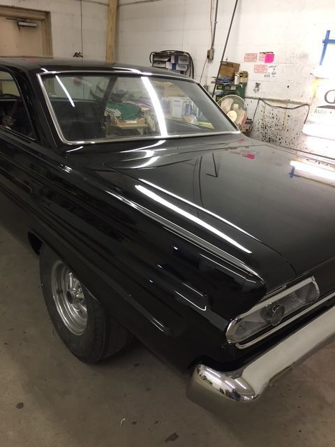 Black classic car in a garage, featuring silver trim and wheels.