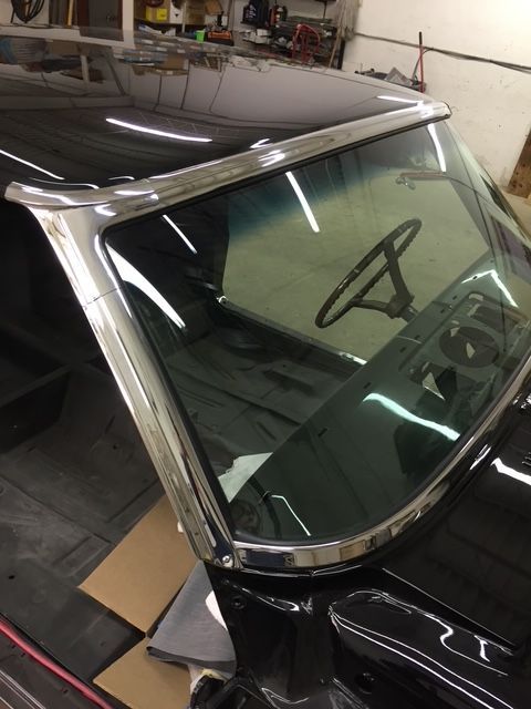 Chrome windshield trim on a black classic car with a steering wheel visible inside.