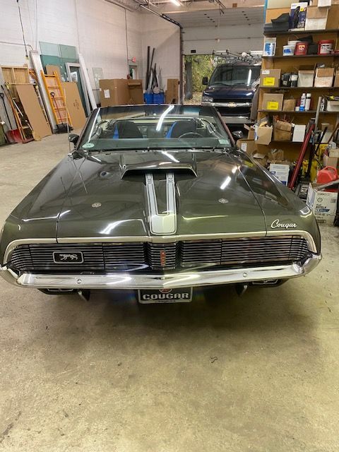 Dark green 1968 Mercury Cougar convertible in a garage. Hood scoop and front license plate visible.