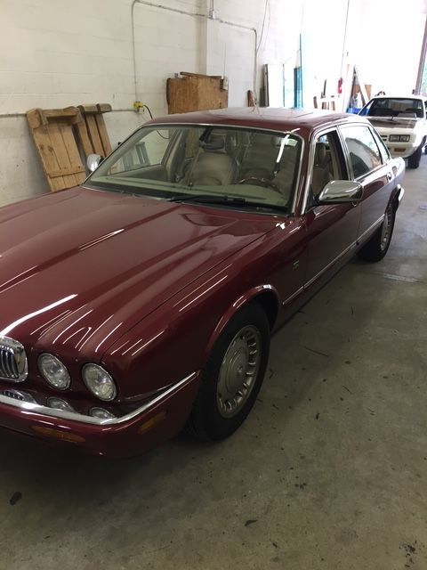 Burgundy Jaguar sedan in a garage, front view. Silver trim, beige interior.