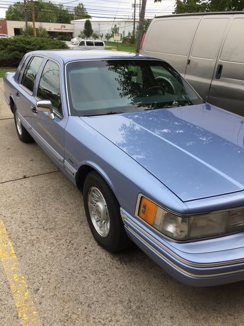 Light blue Lincoln Town Car parked on pavement next to a white van.