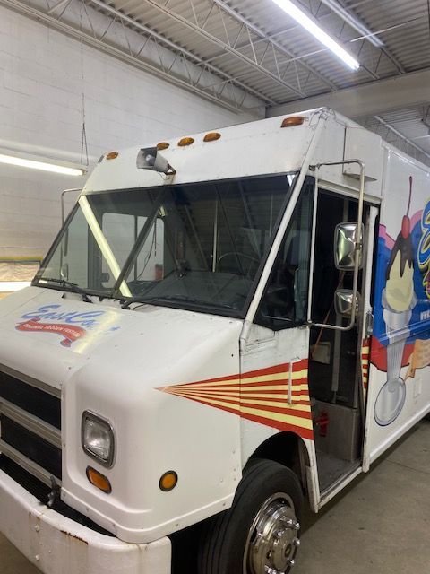 Ice cream truck, white with red and yellow stripes, parked inside, door open.