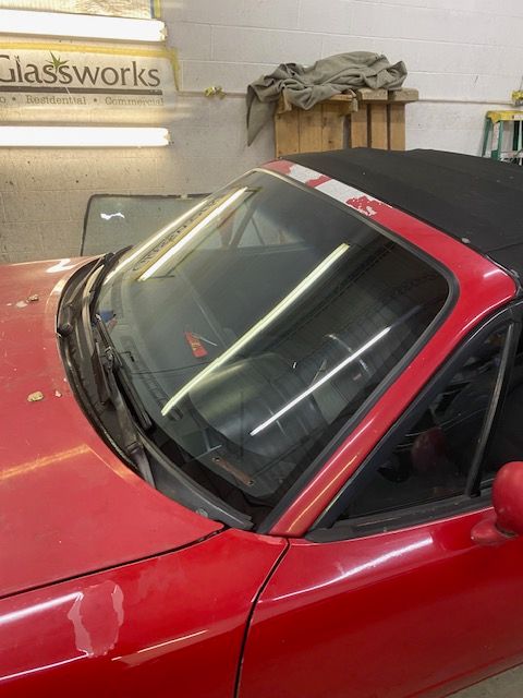 Red convertible car with a cracked windshield inside a shop.