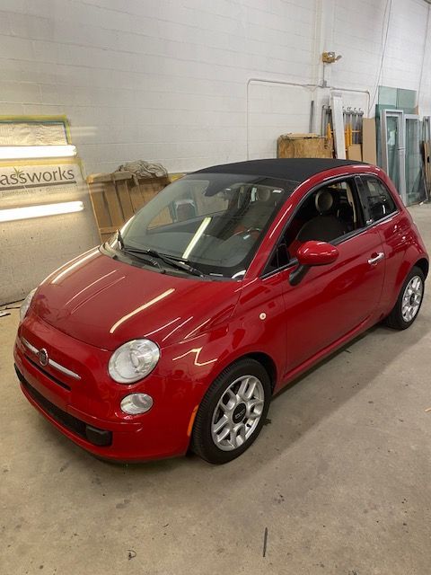 Red Fiat 500 hatchback with a black convertible top, parked inside a garage.
