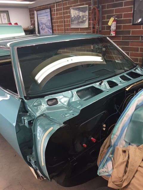A teal classic car in a garage undergoing restoration. The windshield is installed.