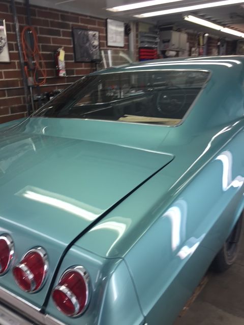 Teal vintage car's rear with tail lights, in a garage setting.