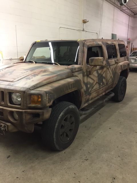 Camouflage Hummer H3 SUV inside a building, likely a garage. The vehicle is brown and grey.