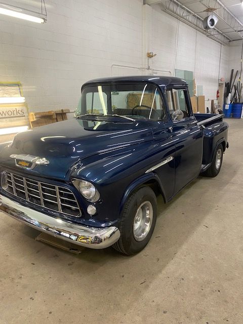 Blue 1957 Chevrolet pickup truck in an indoor setting; chrome trim, silver wheels.