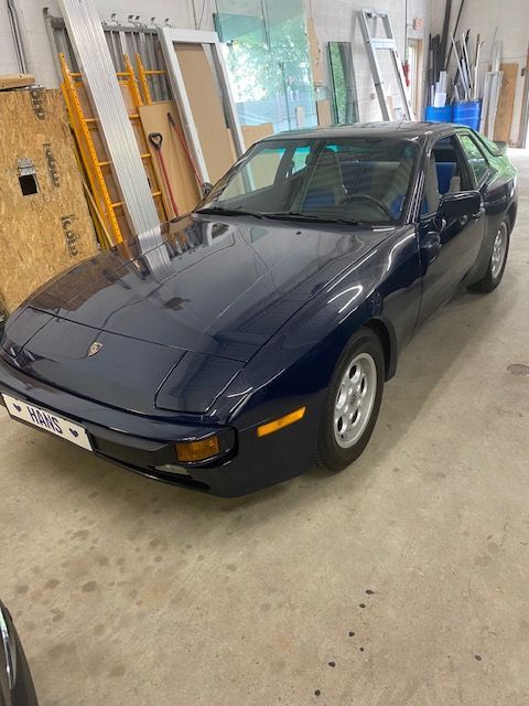 Dark blue Porsche 944 coupe parked inside a garage, with concrete floor.
