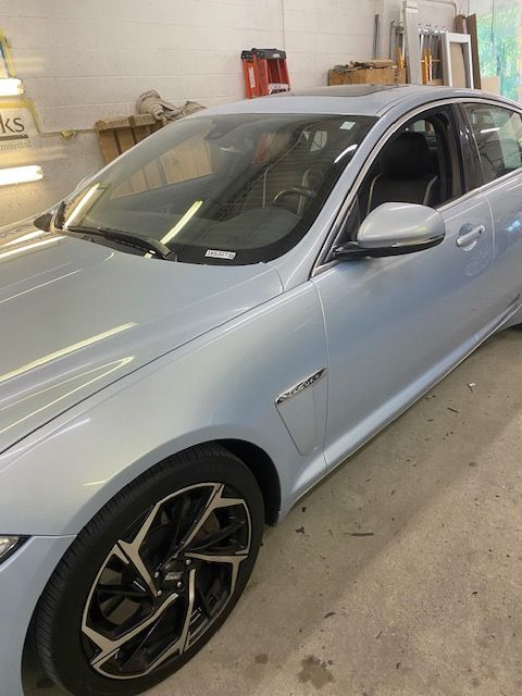 Light blue Jaguar sedan with black and silver rims, parked in a shop setting.