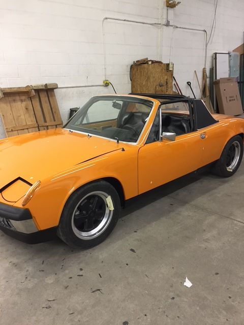 Orange Porsche 914 sports car with black roof and wheels parked inside a building.