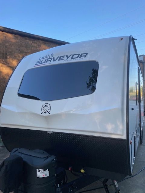 White and black Surveyor travel trailer parked outside, with dark tinted window.