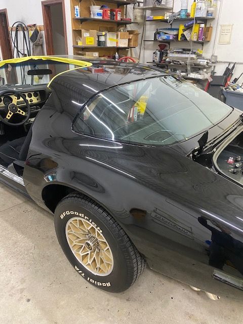Black classic car in a garage, black body, gold wheels, and tinted windows.