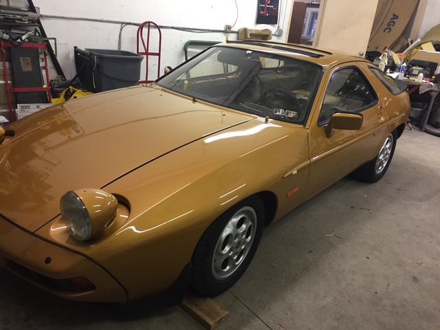 Gold Porsche 928 sports car in a garage.