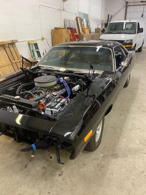 Black classic car with hood open, in a workshop. White van in the background.