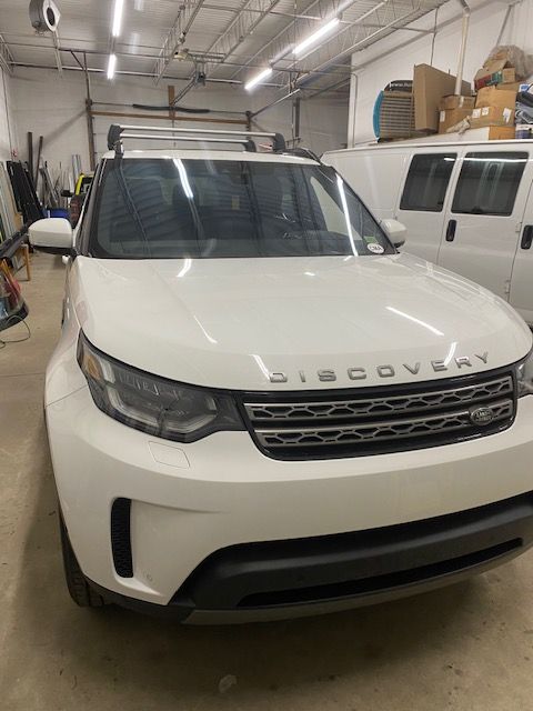 White Land Rover Discovery SUV parked inside a garage; overhead lights.
