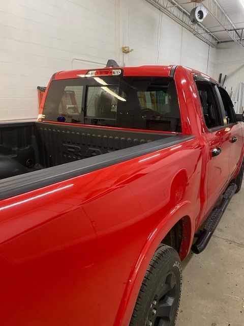 Red pickup truck, side view, parked indoors. Focus on the cab and bed; black tires and rails.