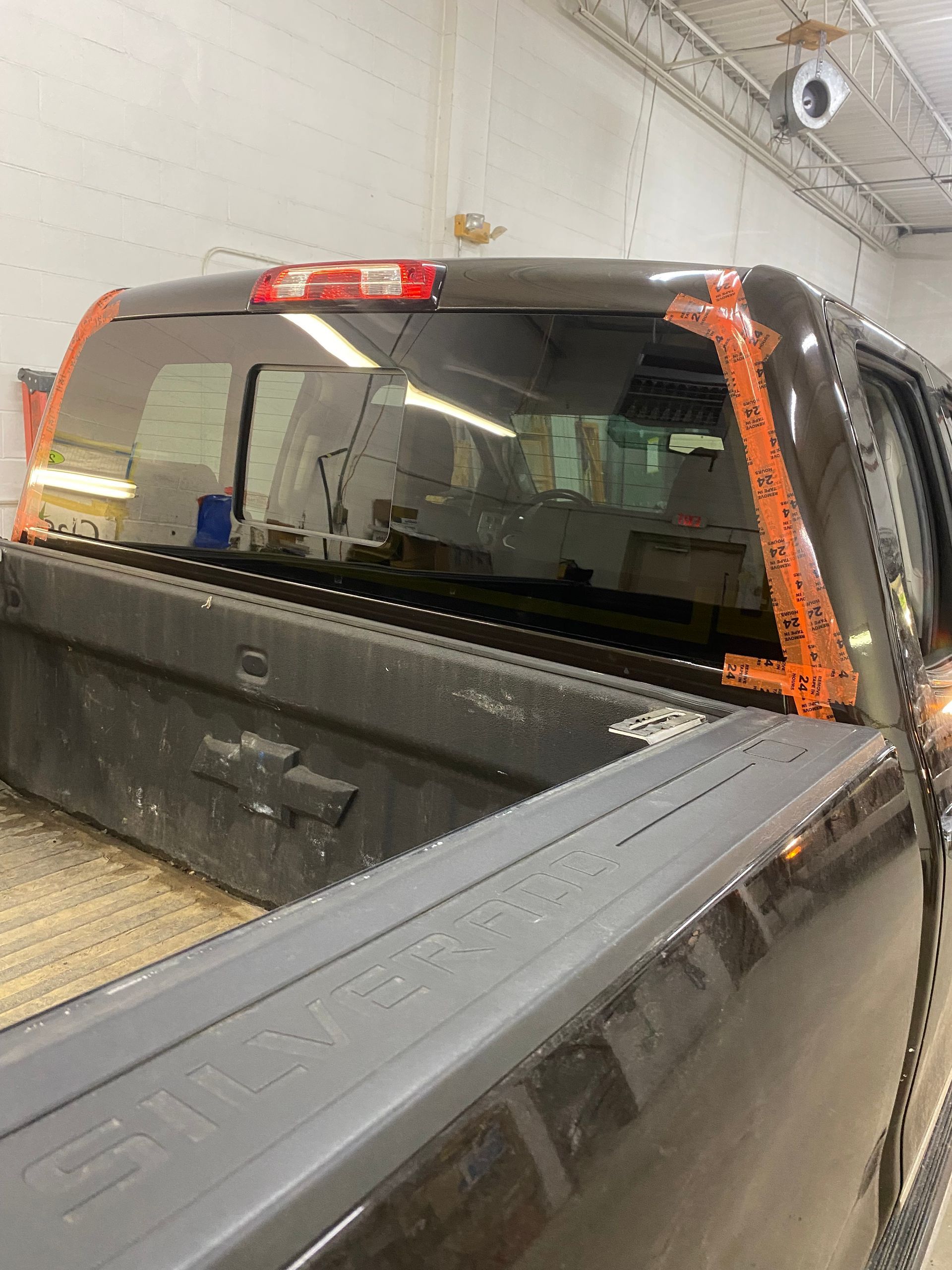 Dark pickup truck bed with rear window taped, orange tape outlining the glass in a garage.