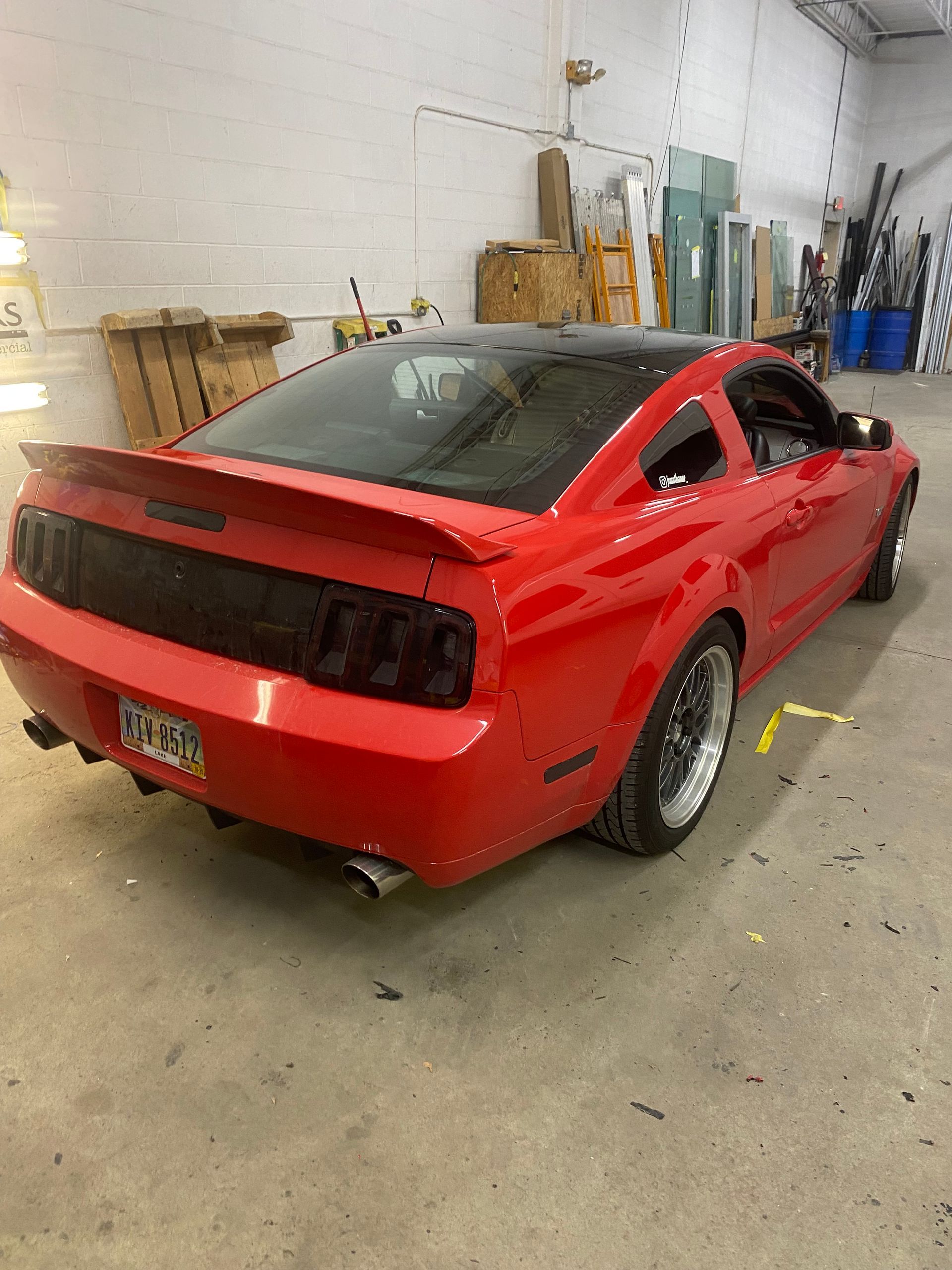 Red Mustang car with black tinted taillights and spoiler inside a garage.