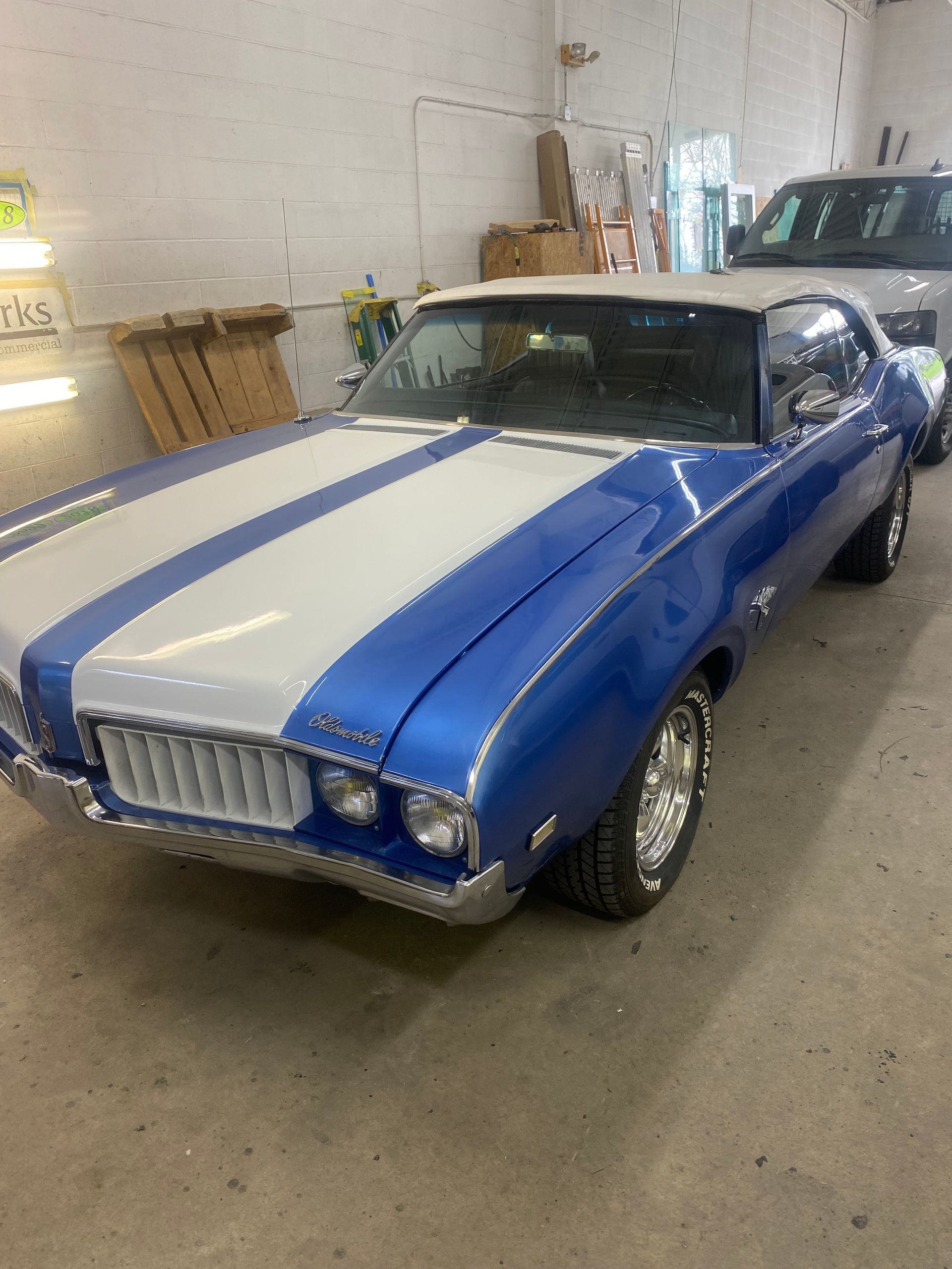 Blue and white classic Oldsmobile convertible with racing stripes parked in a garage.