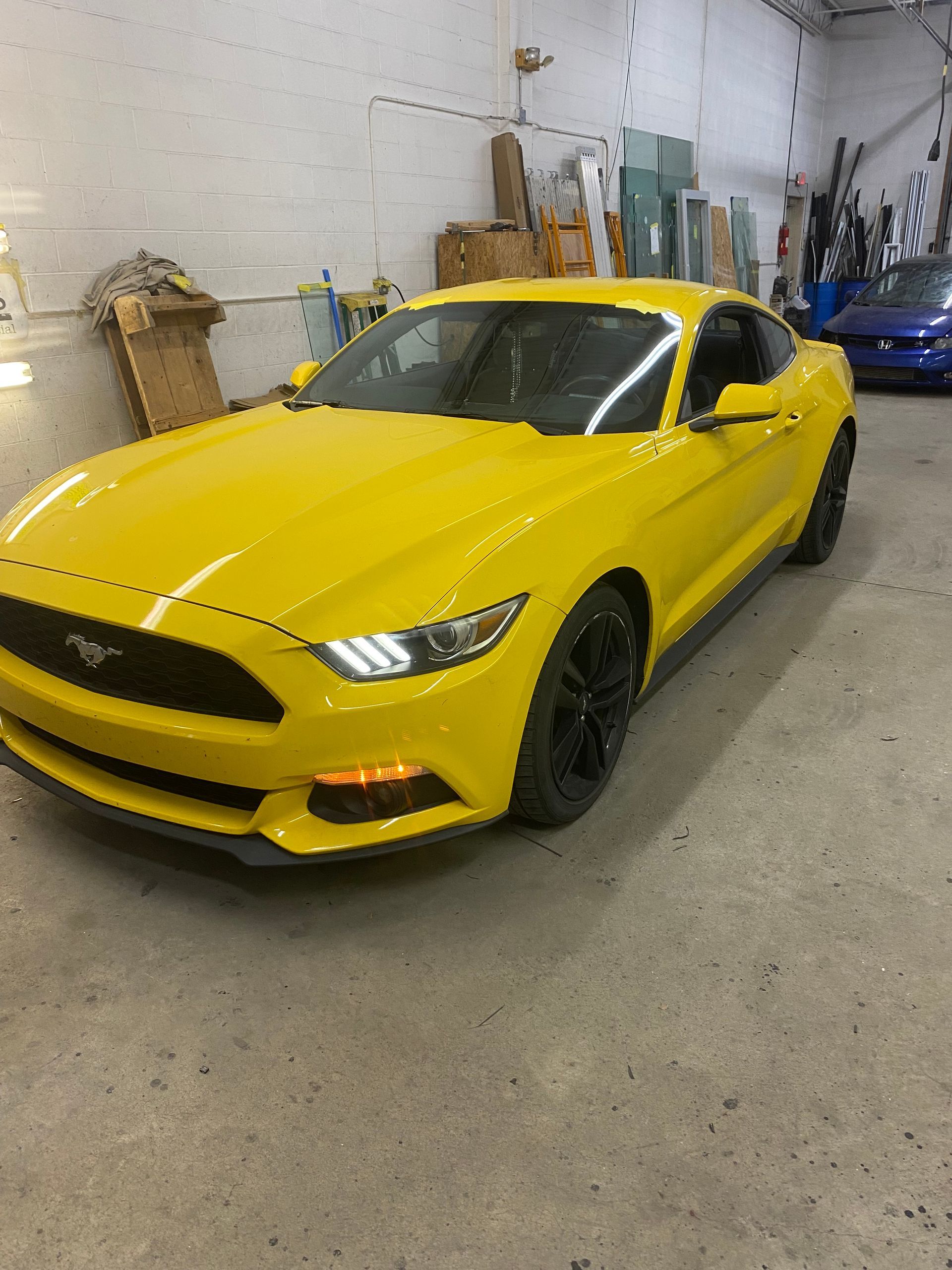Yellow Ford Mustang parked in a garage with a blue car in the background.