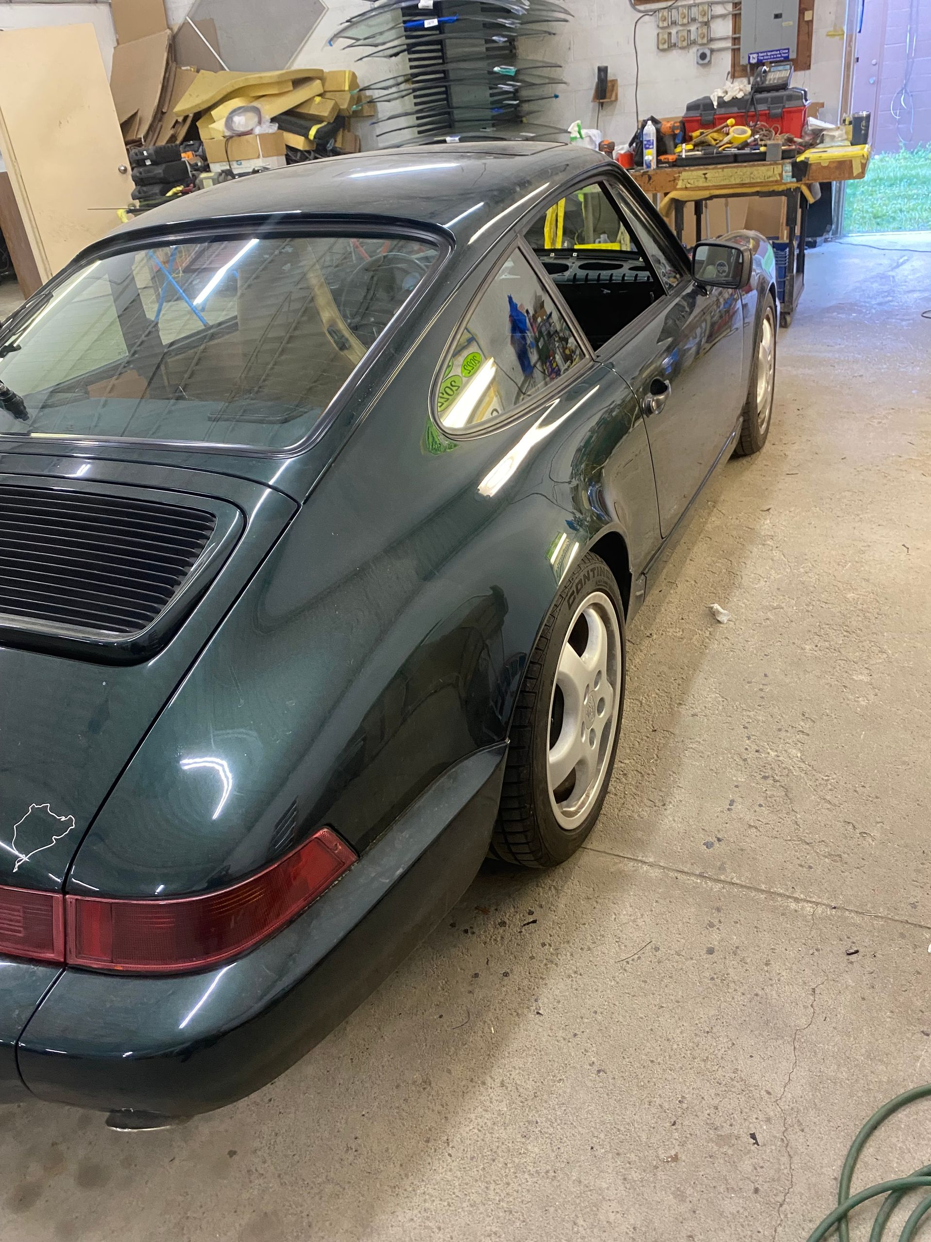 Dark green Porsche 911 coupe parked in a garage, rear quarter view.
