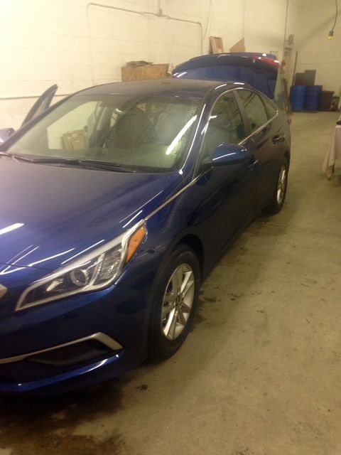 Blue sedan car parked inside a garage with its doors and trunk open.