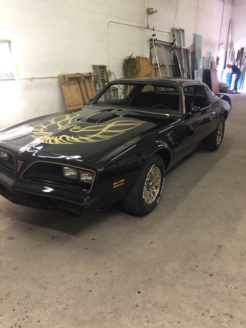 Black Pontiac Firebird Trans Am with gold hood bird logo in a garage.