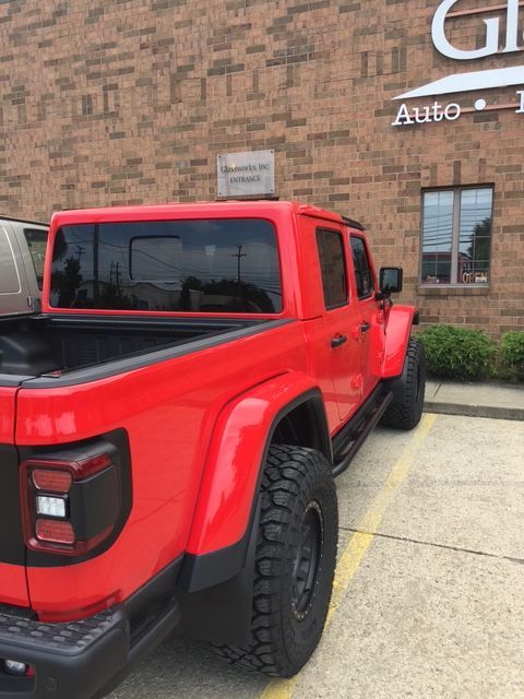 Red Jeep Gladiator truck parked outside a brick building with a business sign.