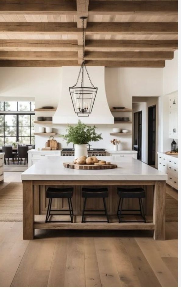 Spacious kitchen with wood beams, white counters and cabinets, and an island with stools.