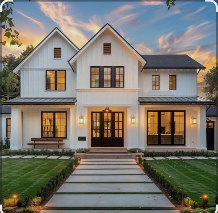 White farmhouse with black windows and doors, pathway leading to entrance, green lawn, evening sky.