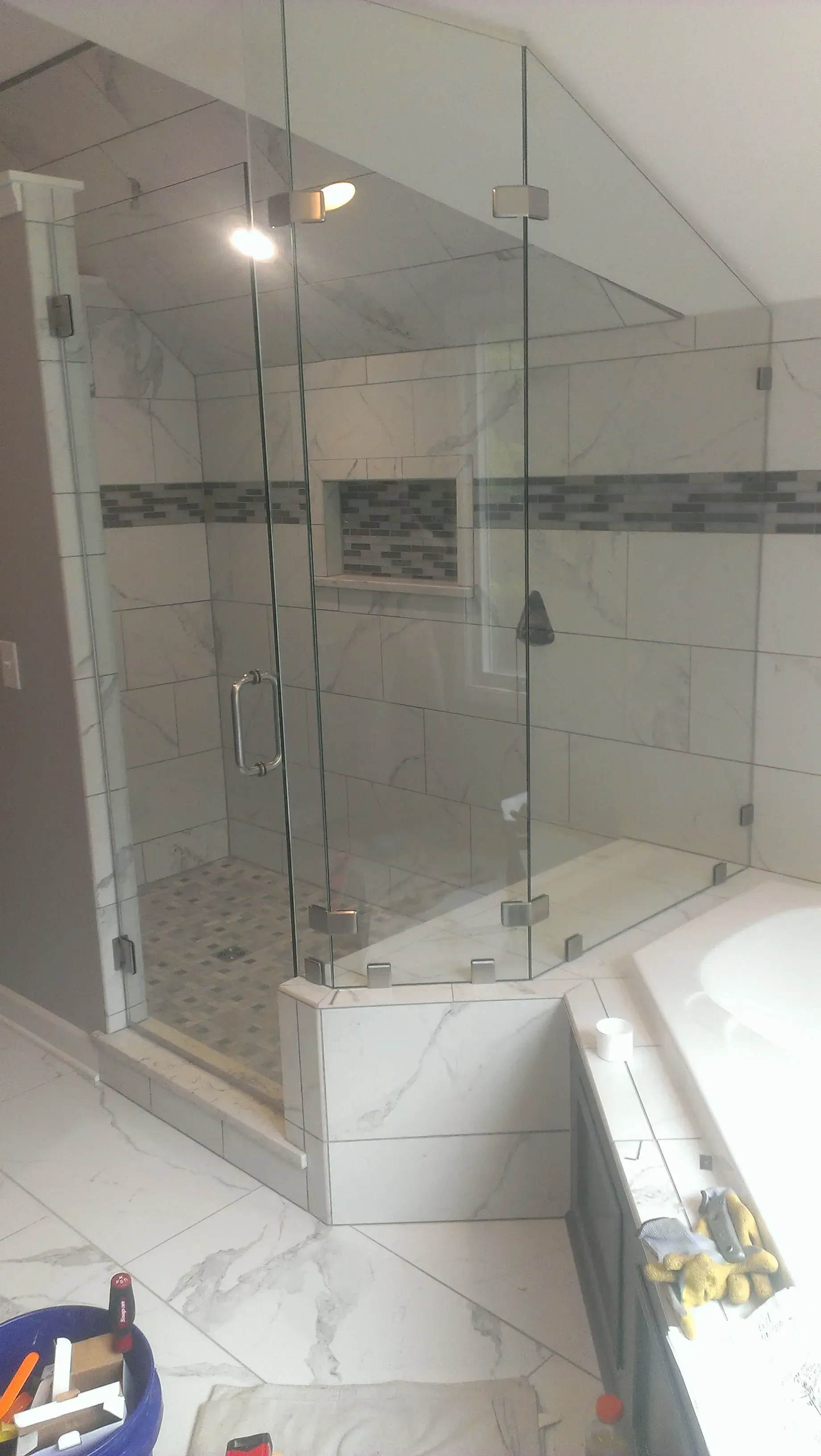 Glass-enclosed shower with marble tile, a built-in seat, and a recessed shelf.
