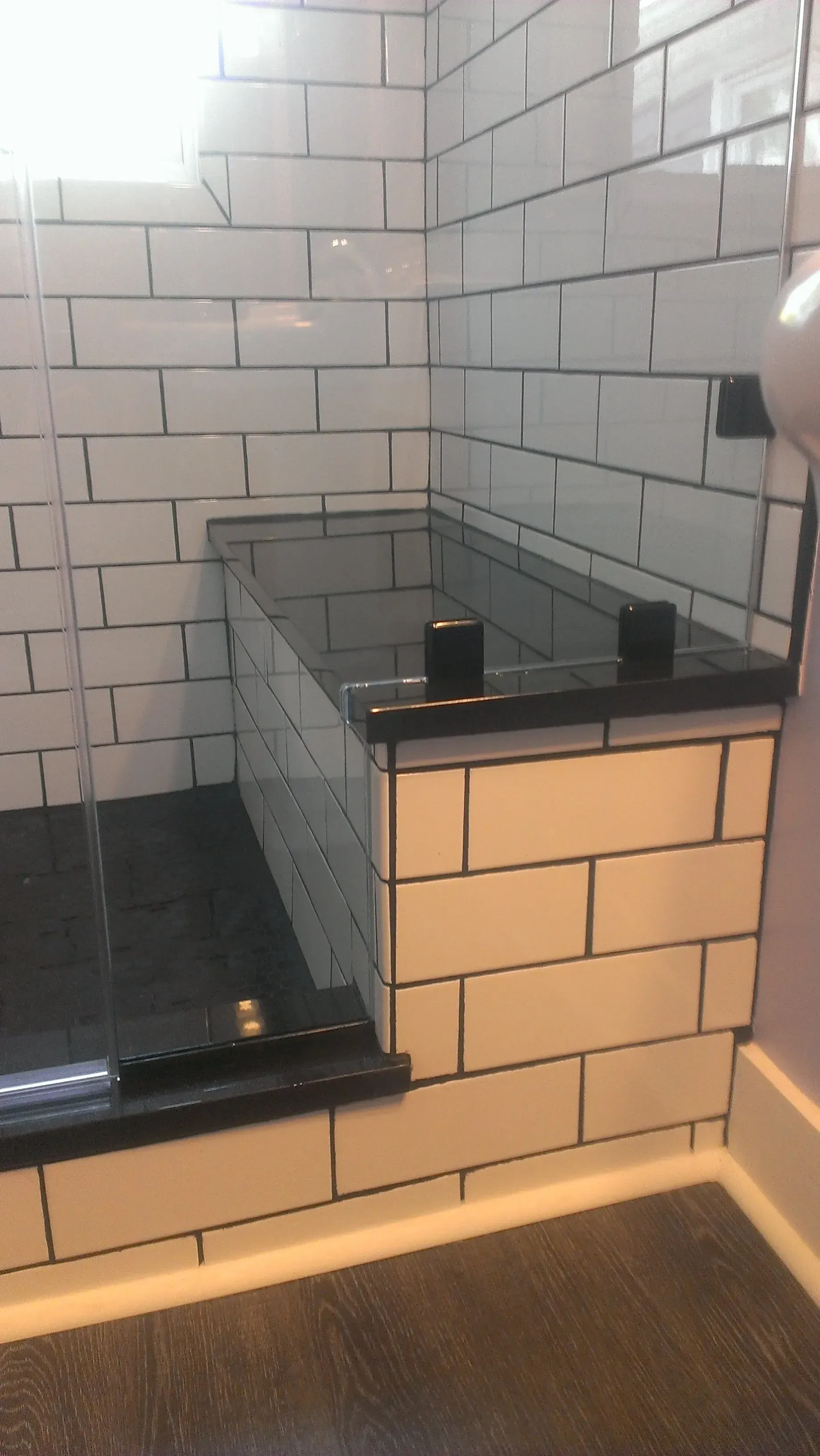 White tiled shower with black accents, including a seat and glass door.