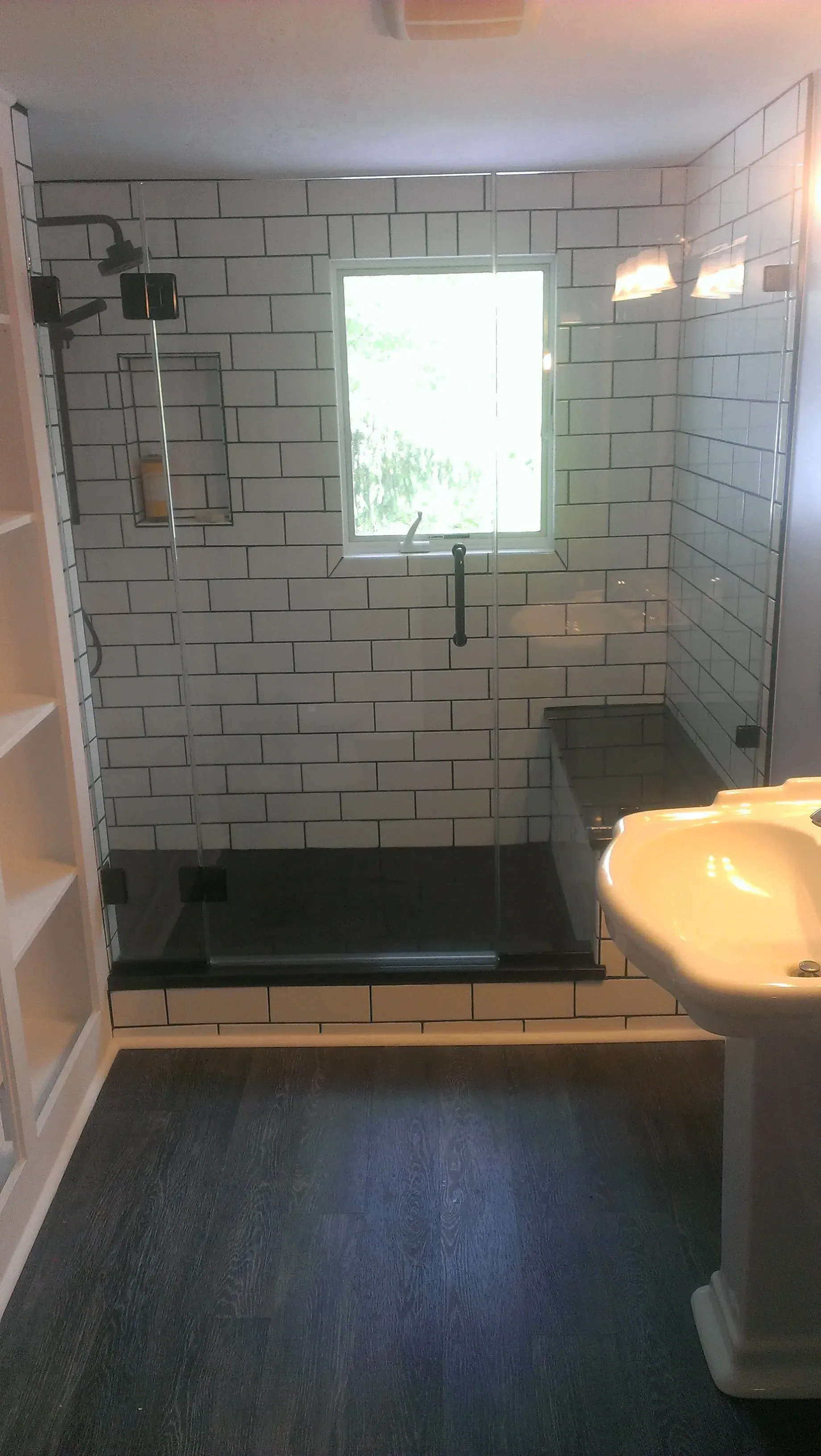 Modern bathroom with black and white tile shower, glass door, sink, and window.
