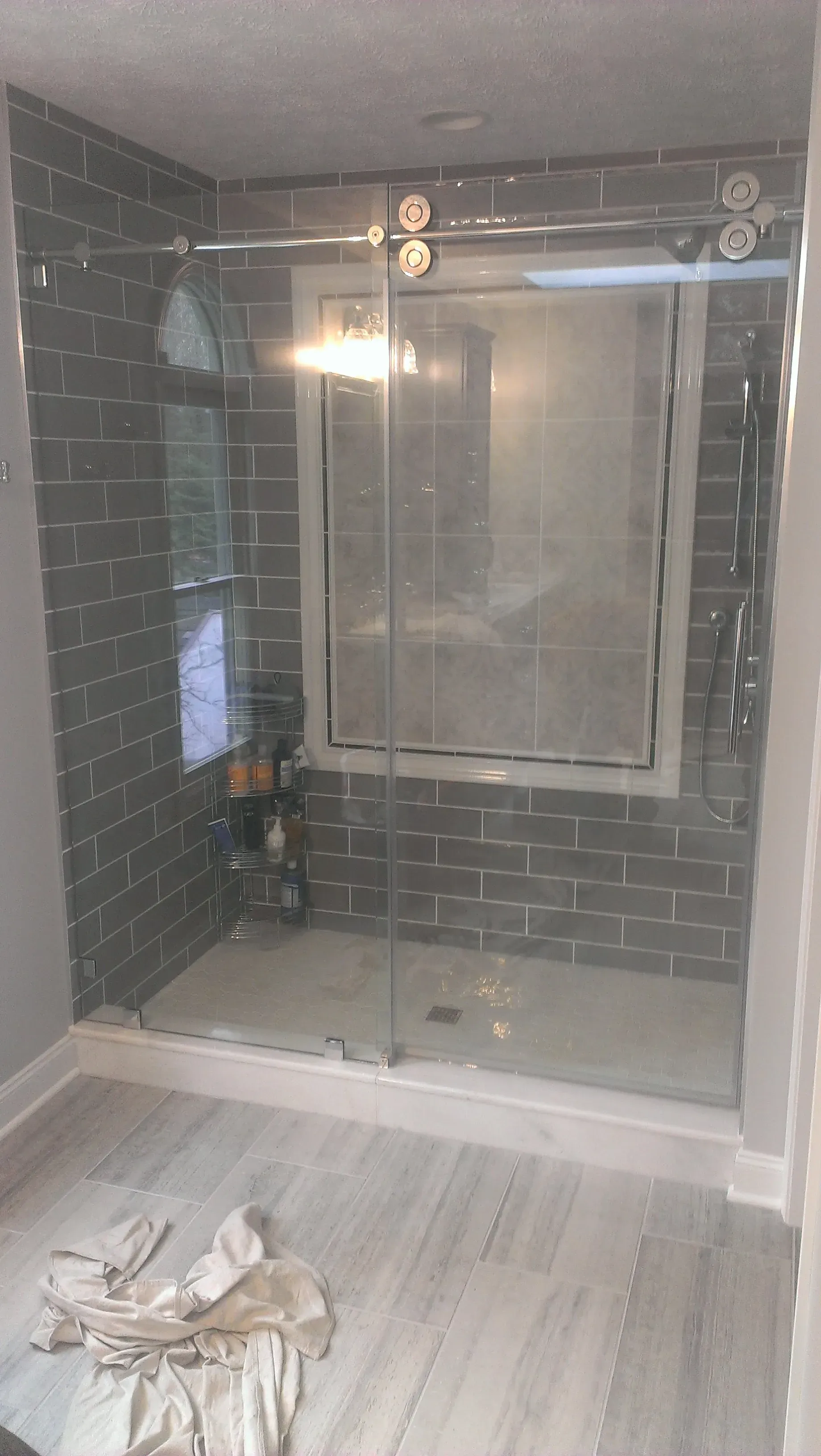 Modern bathroom with dark gray tiled shower, glass doors, and light wood-look flooring.