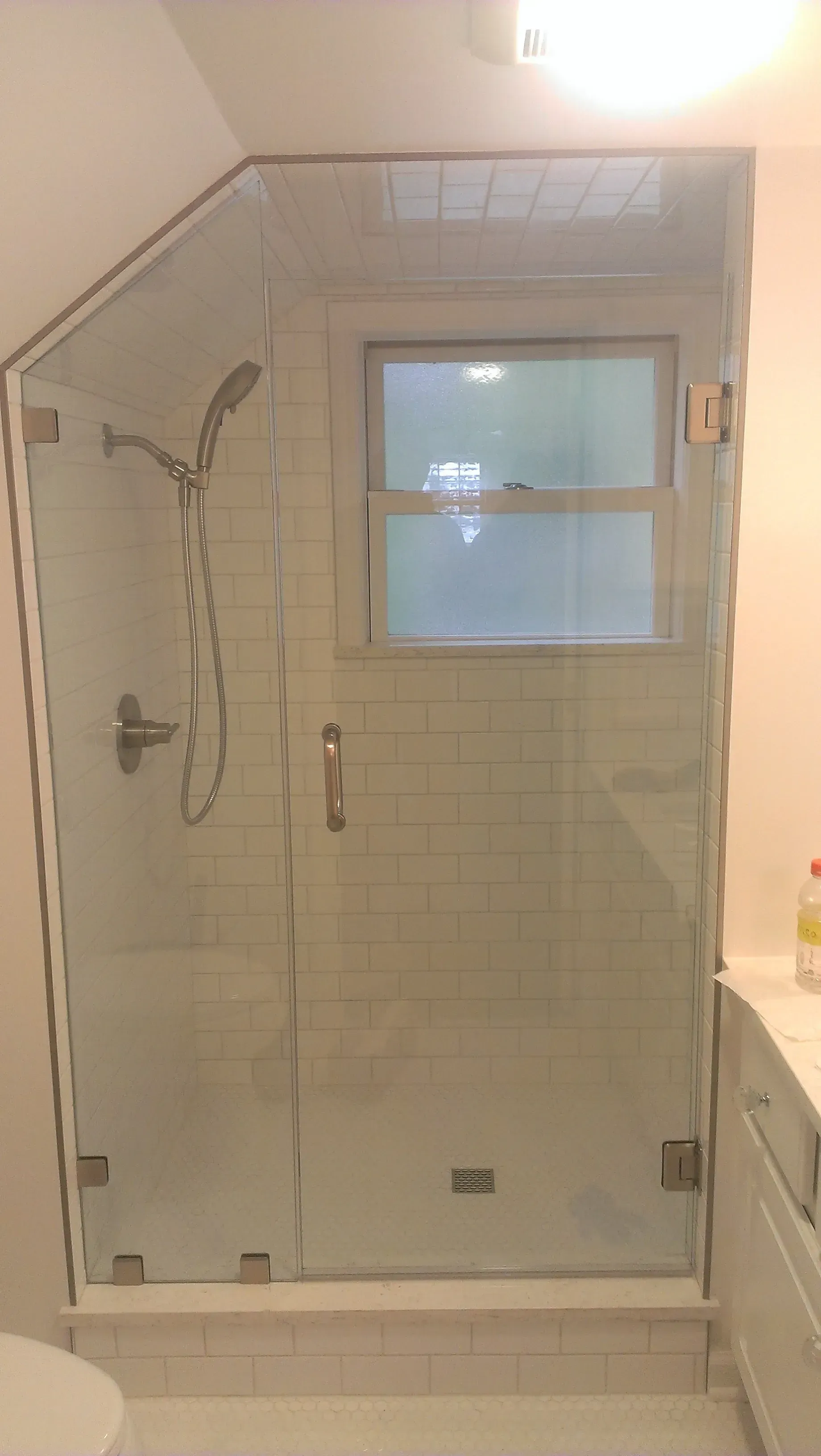 Glass shower enclosure with a window, white tiles, and silver fixtures in a bathroom.