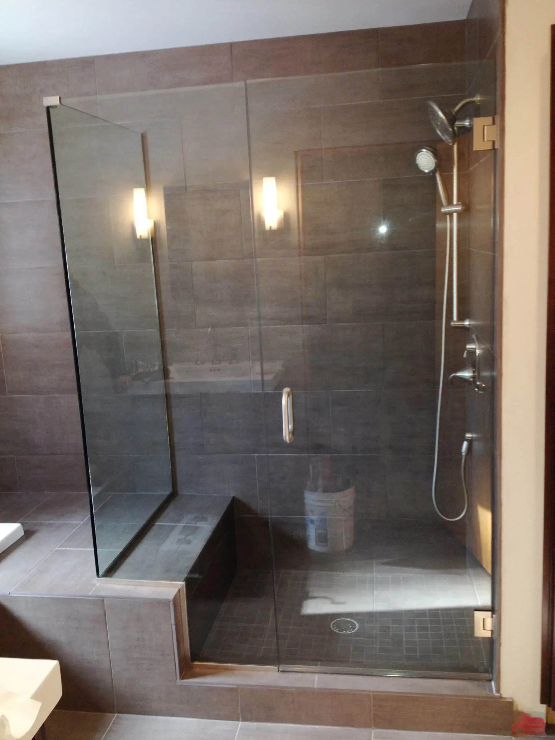 Glass shower with a bench, dark tile walls, and chrome fixtures.