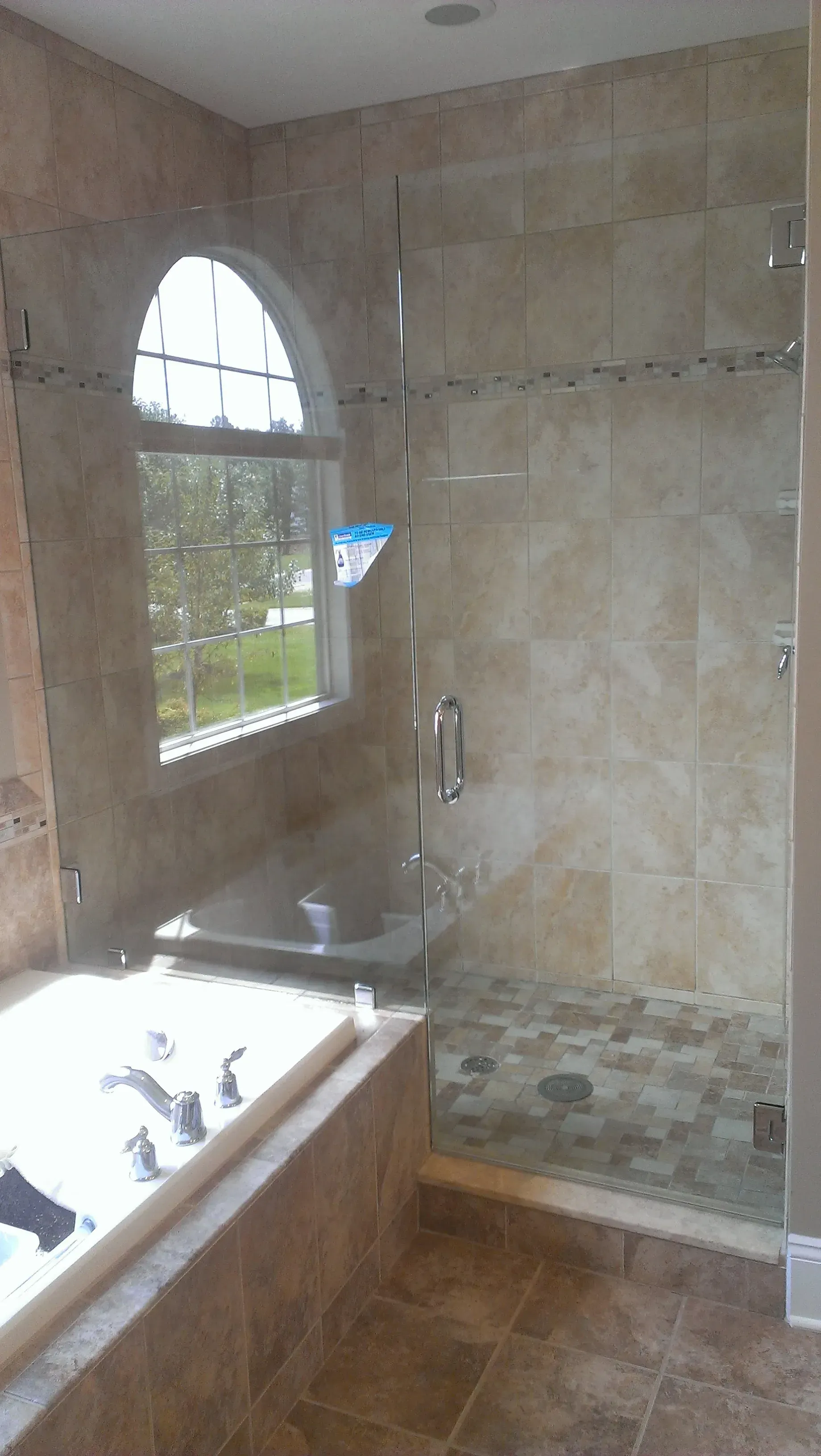 Bathroom with a glass shower enclosure, beige tile, and a window.