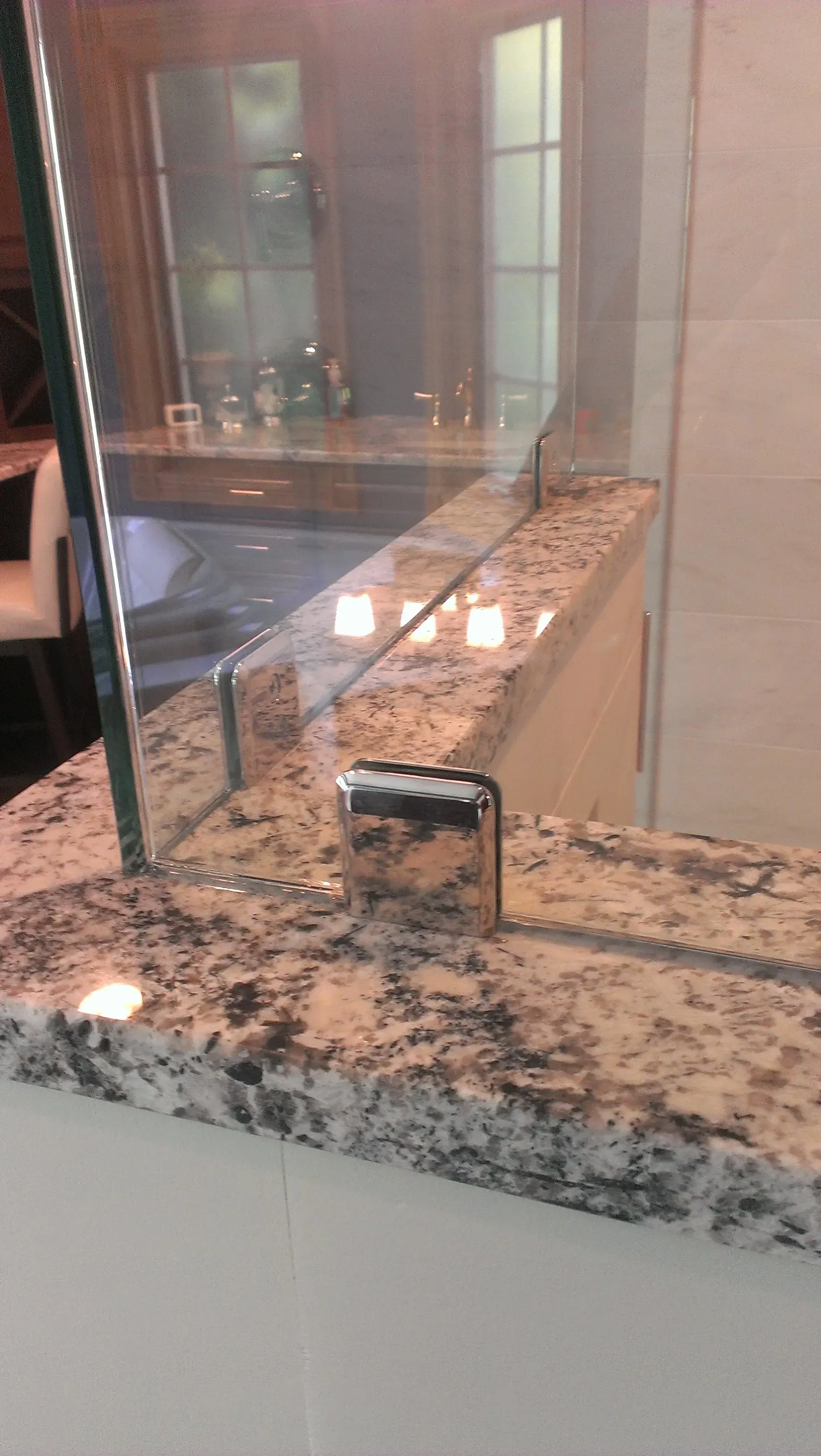 Granite countertop with glass shower wall and chrome supports. Interior shot with a mirror reflection.