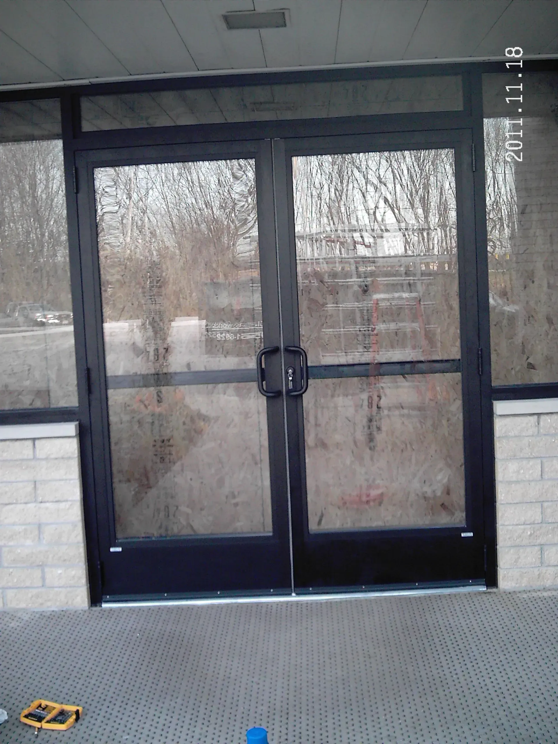 Black double doors with glass panels, in front of a light-colored brick building.