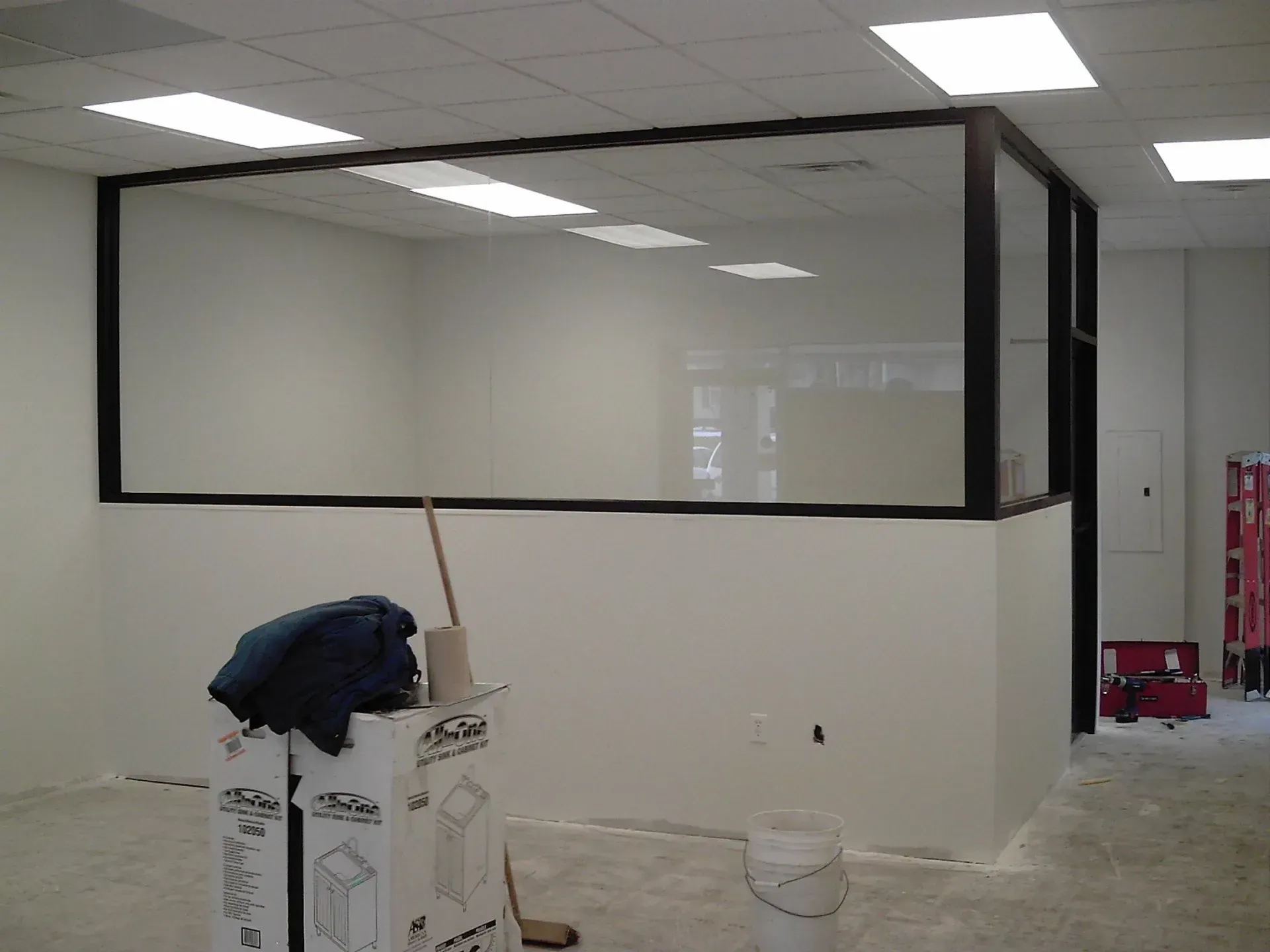 Interior of a room with white walls, a glass partition, and construction materials on the floor.