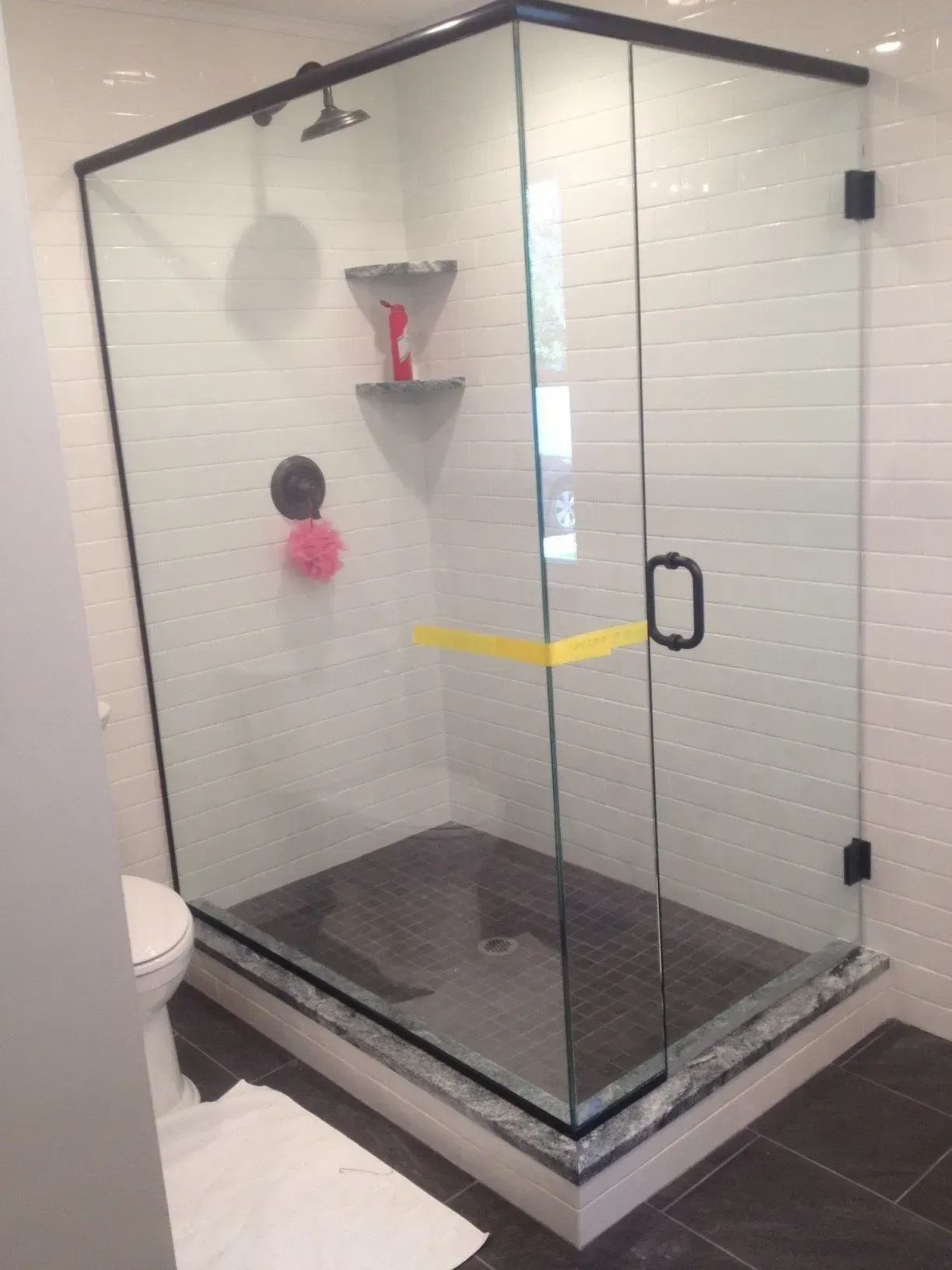 Glass shower with black trim, dark tiled base, white tiled walls, and black door handle.